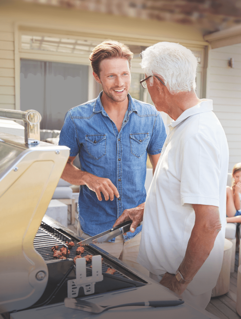 man cooking meat on the grill while talking to a friend
