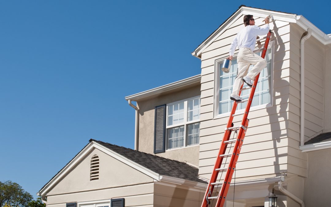 A house painter with a paintbrush doing an exterior paint job.